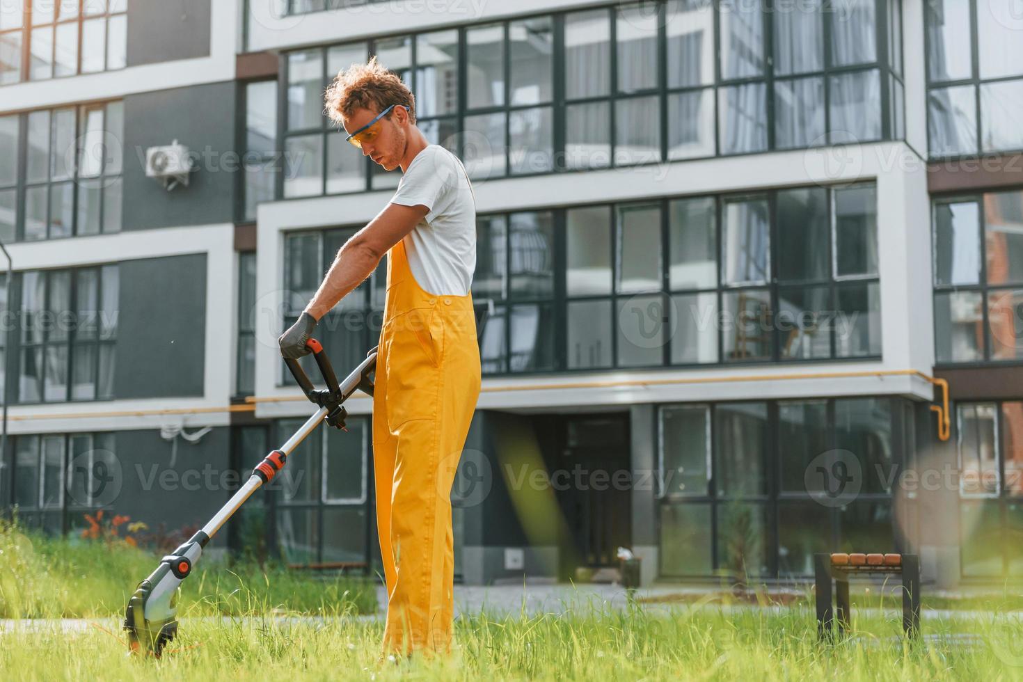 bezig dag. Mens besnoeiing de gras met gazon verhuizer buitenshuis in de werf foto