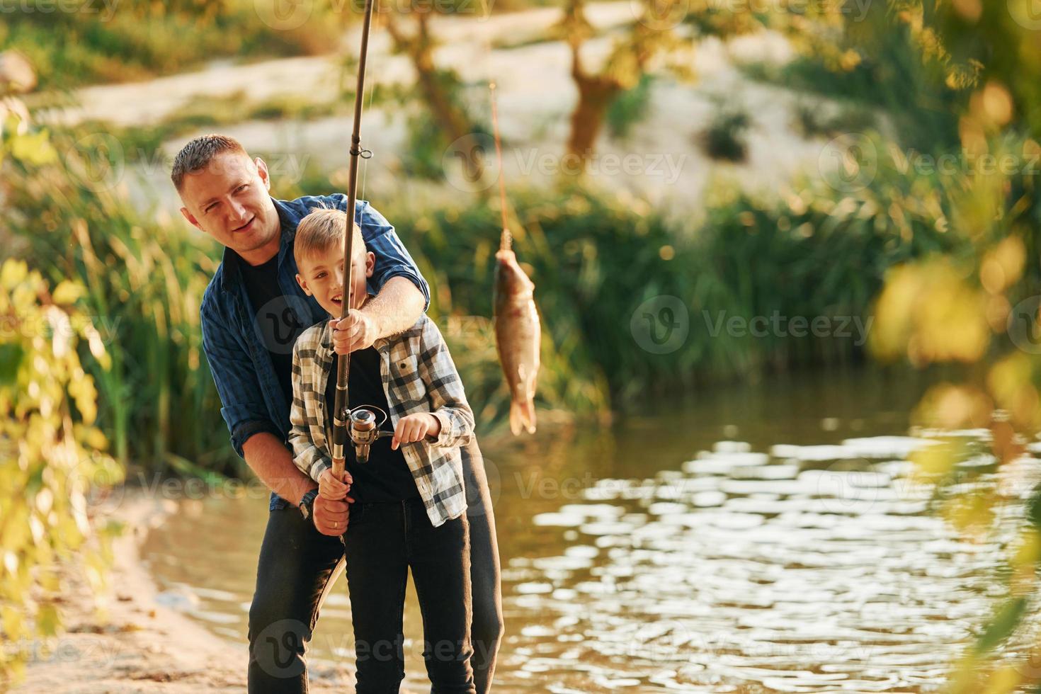 Holding de vangst. vader en zoon Aan visvangst samen buitenshuis Bij zomertijd foto