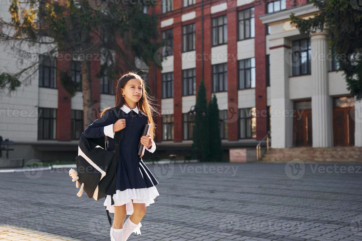 hebben een wandelen. schoolmeisje is buiten in de buurt school- gebouw foto