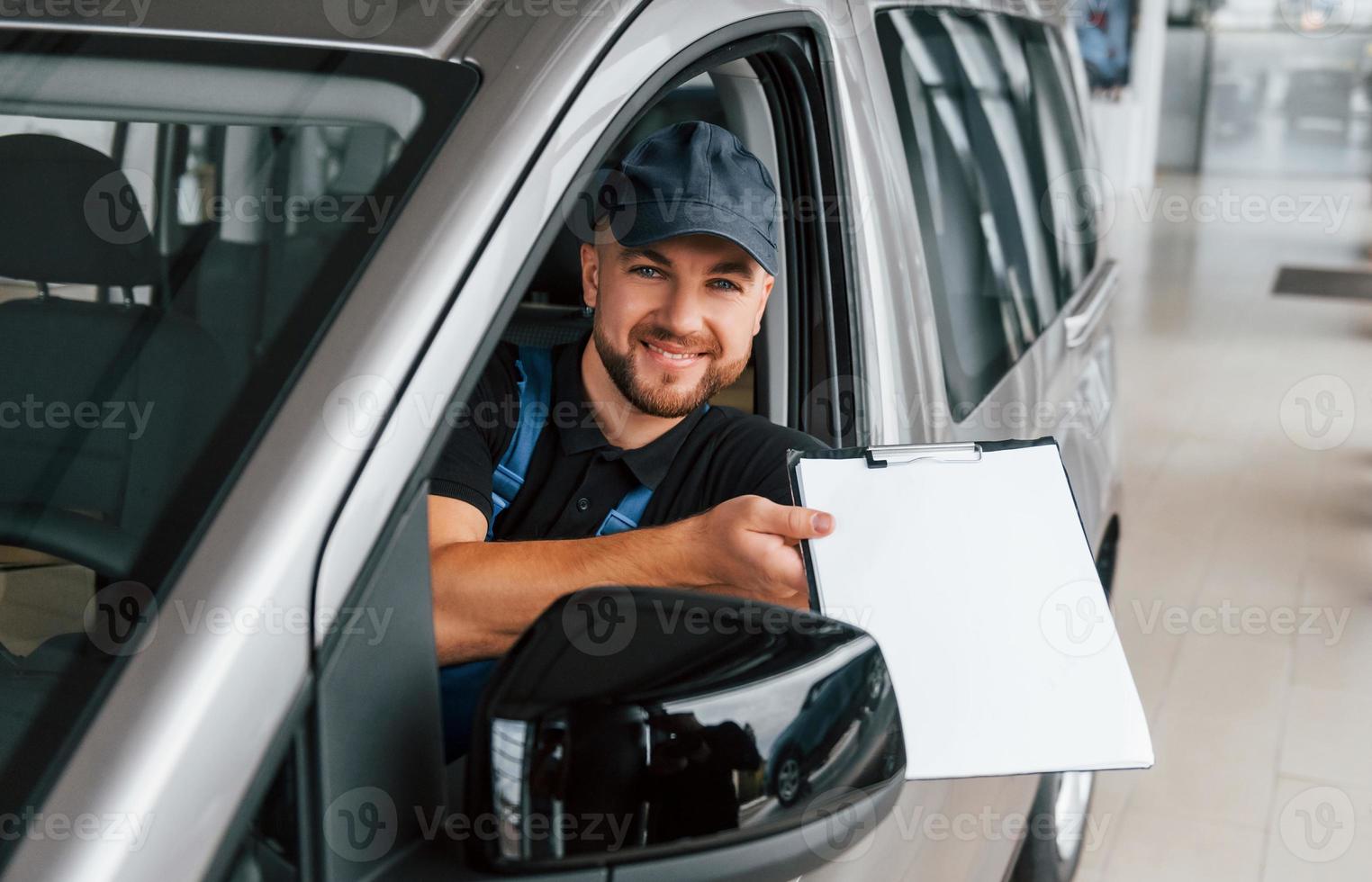 zittend in voertuig en Holding document. levering Mens in uniform is binnenshuis met auto en met bestellen foto