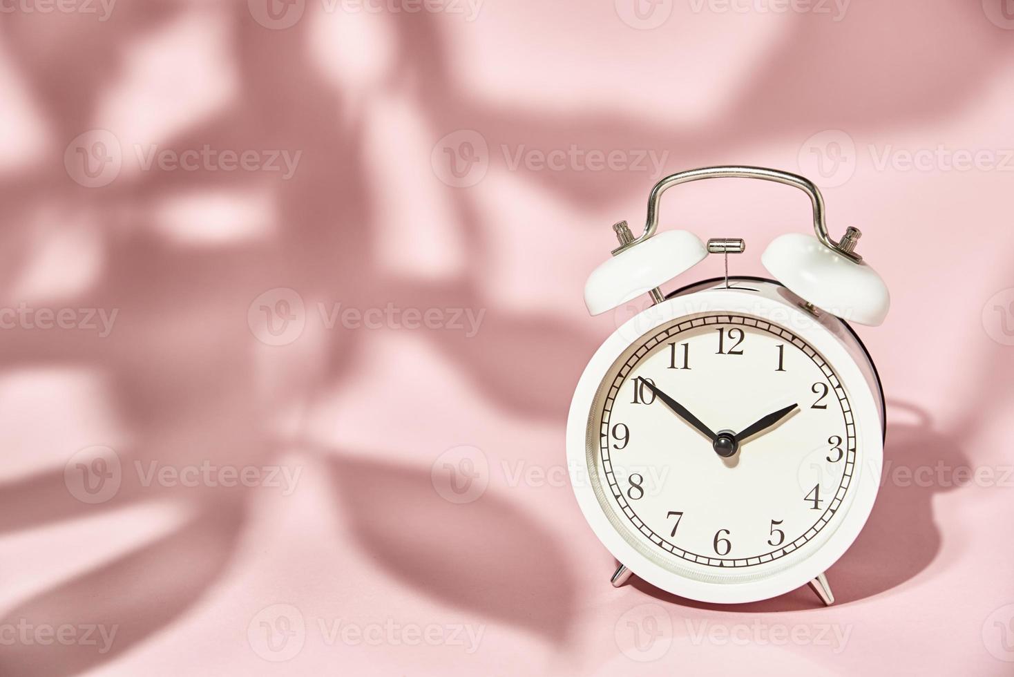 wit alarm klok en bladeren schaduwen Aan pastel roze achtergrond foto