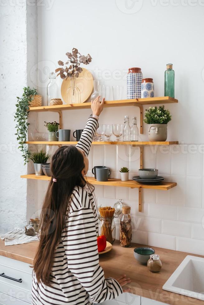 vrouw duurt uit een glas van plank in de keuken foto