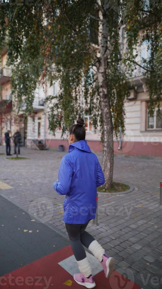 achterzijde visie van een volwassen vrouw rennen buitenshuis Aan een straat foto