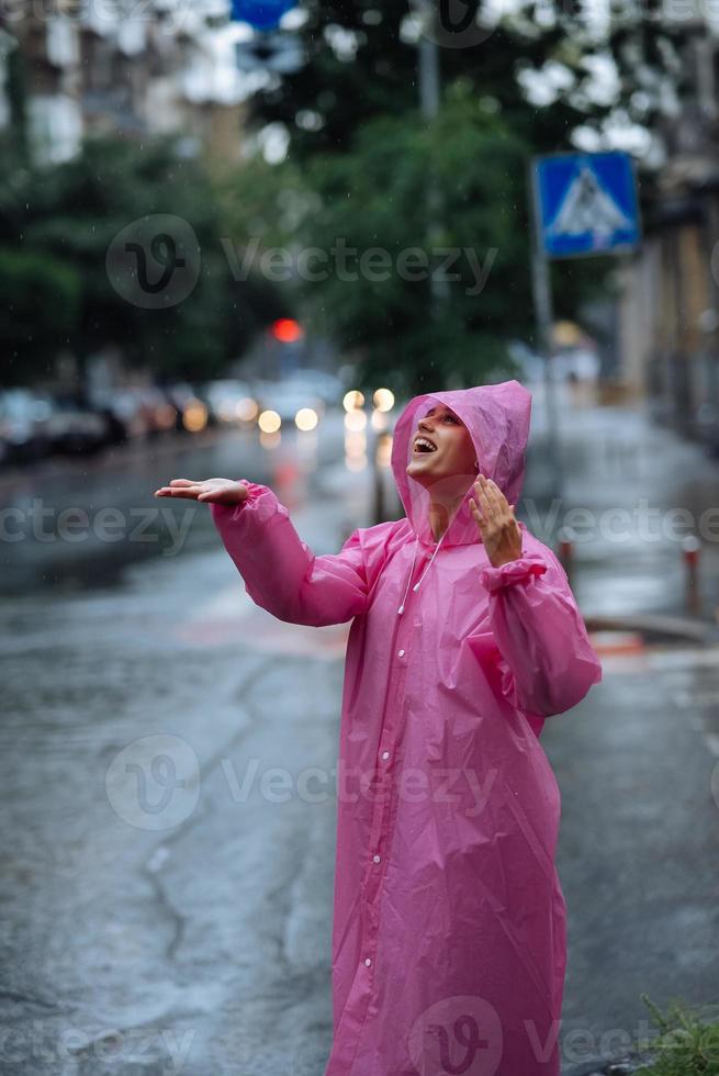 jong glimlachen vrouw met regenjas terwijl genieten van een regenachtig dag. foto