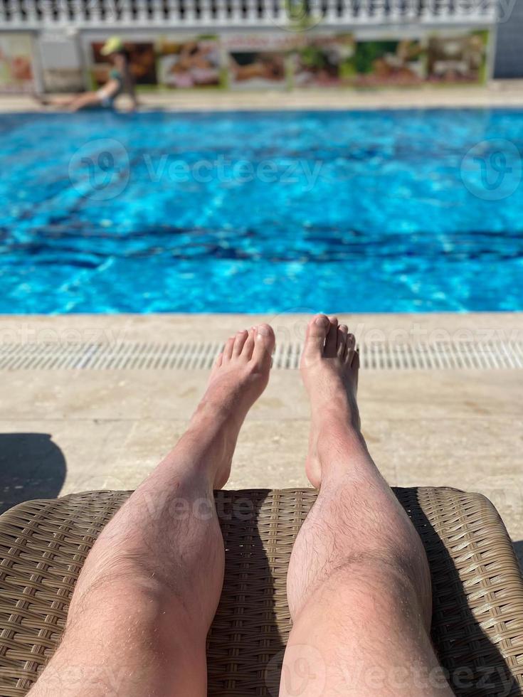 poten van Mens - mannetje toerist leugens Aan een strand stoel gedurende zonsondergang in de zwemmen zwembad Oppervlakte van de hotel faciliteit foto