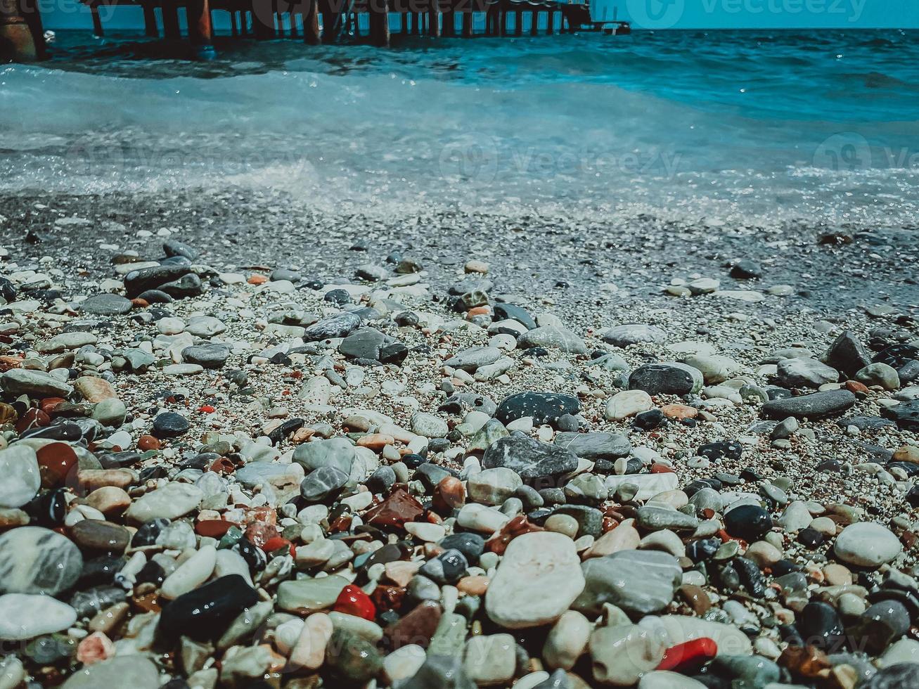 vakantie door de zee Aan de strand. kiezelsteen strand met stenen. nat, klein, veelkleurig stenen in de buurt de water, golven met wit schuim foto
