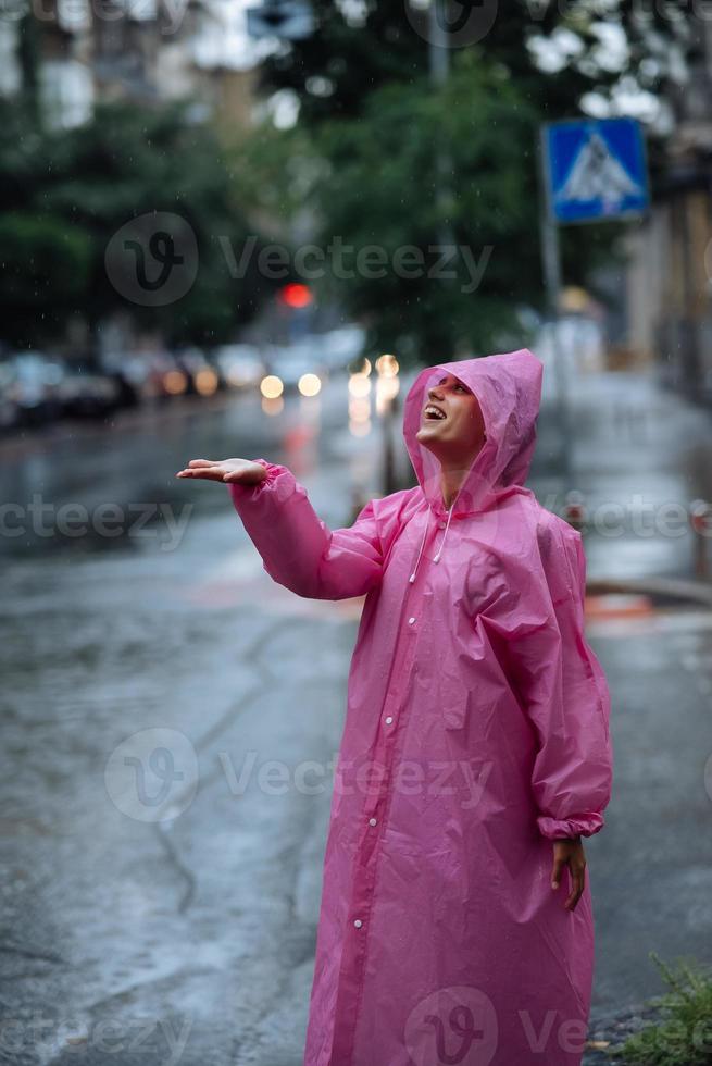 jong glimlachen vrouw met regenjas terwijl genieten van een regenachtig dag. foto