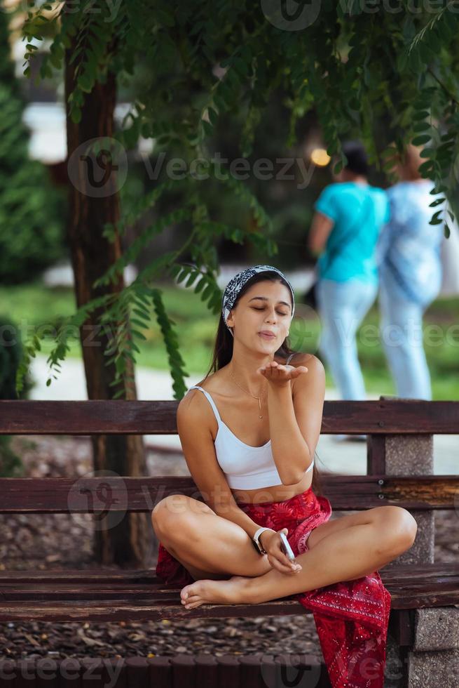 vrouw gebruik makend van een smartphone in park zittend Aan een bank foto