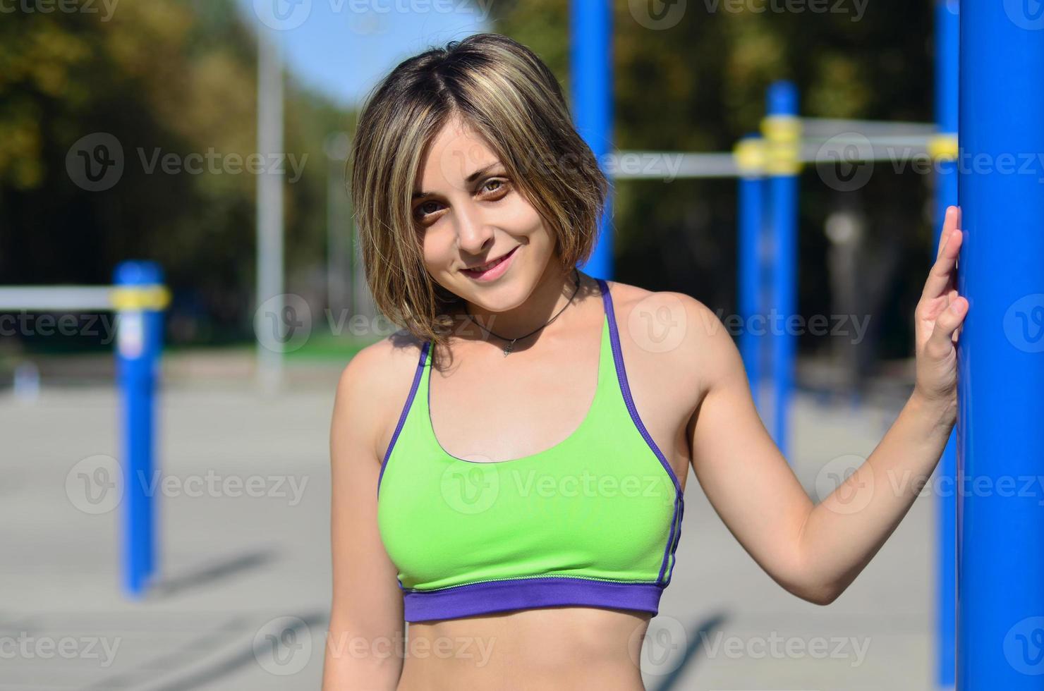 portret van een jong Kaukasisch atleet meisje in een helder groen sportkleding tegen de backdrop van een straat sport- Sportschool voor buitenshuis atletiek opleiding. zomer sport- in de Open lucht foto