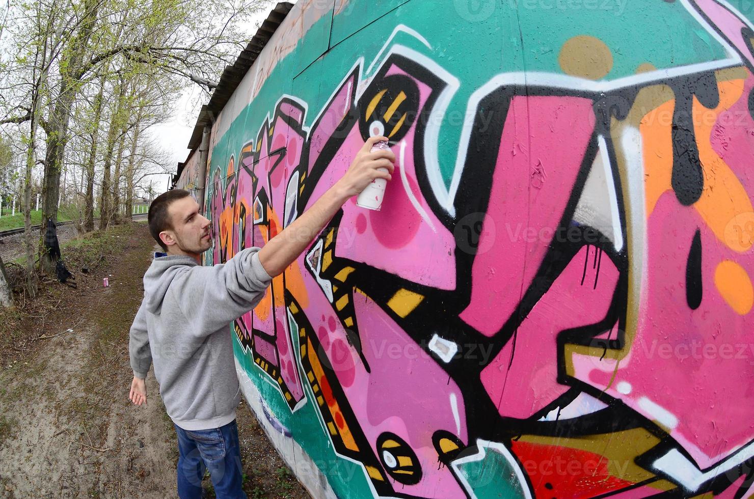 een jong vent in een grijs capuchon verven graffiti in roze en groen c foto