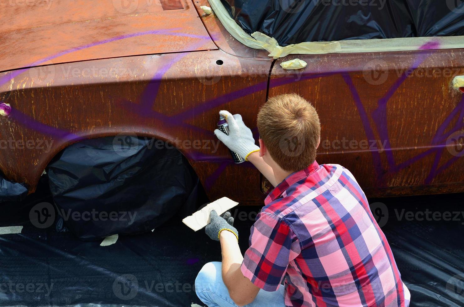 een jong roodharig graffiti artiest verven een nieuw kleurrijk graffiti Aan de auto. foto van de werkwijze van tekening een graffiti Aan een auto detailopname. de concept van straat kunst en onwettig vandalisme