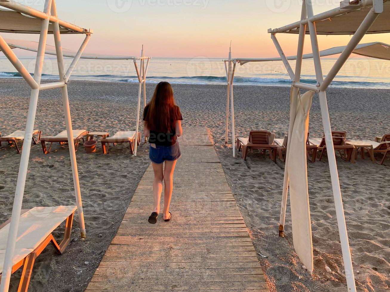 de meisje gaat naar de zee Aan de strand Bij de zee Verleden de zon paraplu's en dek stoelen in de hotel Aan vakantie in een paradijs warm oostelijk tropisch land toevlucht foto