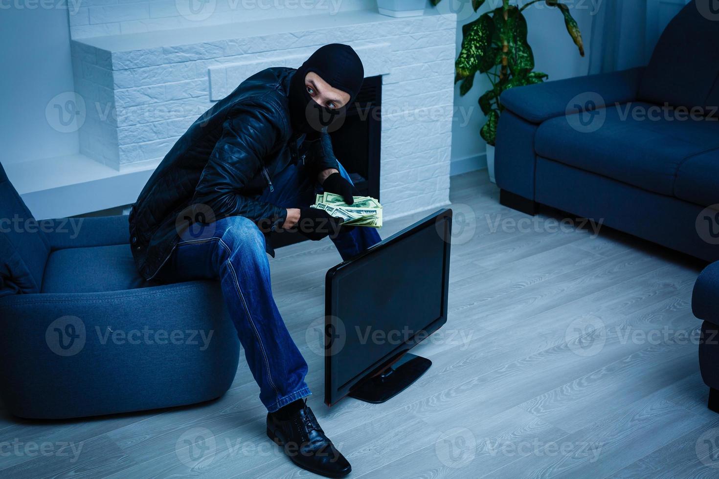 rover Mens gekleed in zwart capuchon staat met vermomd gezicht en houdt een veel van geld in zijn handen, stal een groot hoeveelheid, een dief Mens stal een TV foto