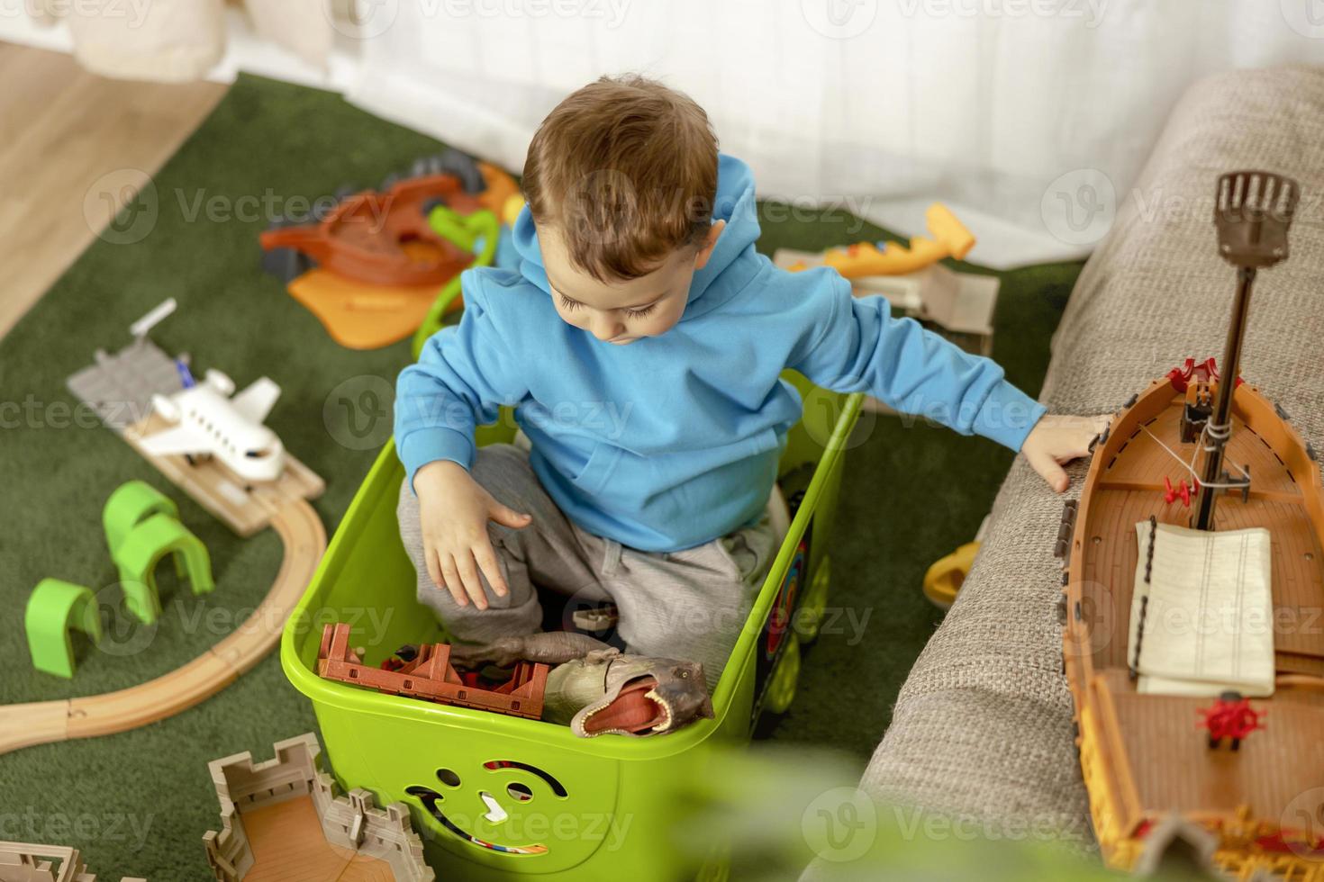 weinig Kaukasisch jongen met blauw capuchon spelen met kleurrijk speelgoed Bij huis. kind hebben plezier. gelukkig en vrolijk kind Toneelstukken met schip, dinosaurussen, kasteel. vrije tijd werkzaamheid, huiselijk leven. selectief focus foto