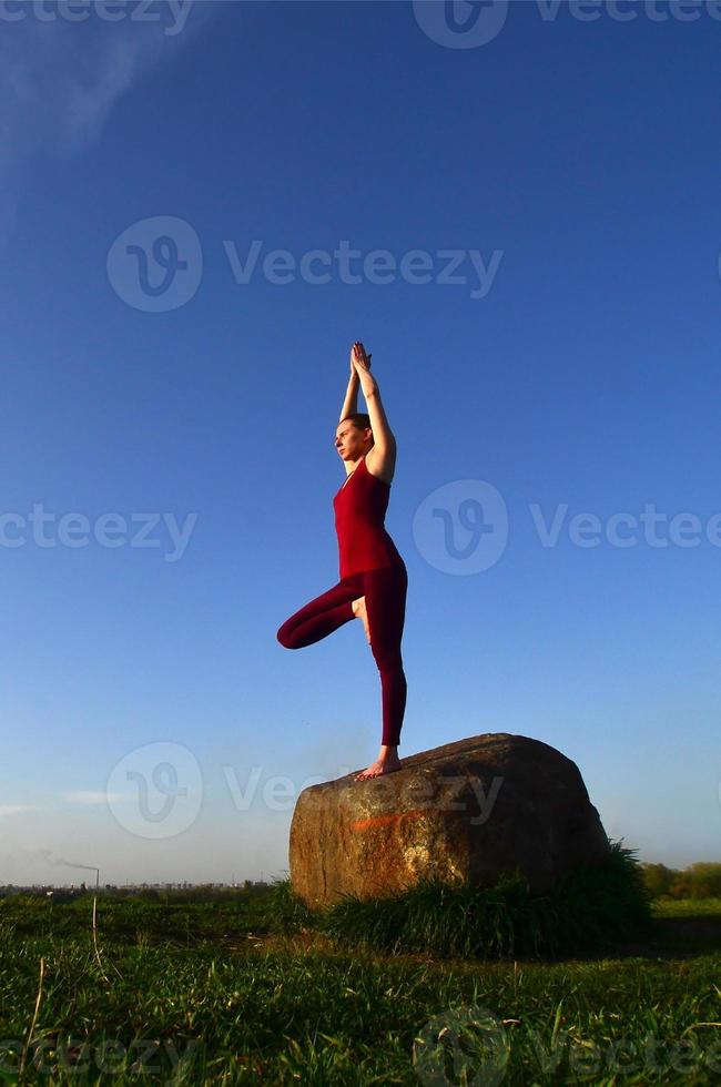 silhouet van jong blond meisje in sport pak praktijk yoga Aan een pittoreske groen heuvel in de avond Bij zonsondergang. de concept van oefenen en gezond levensstijlen foto