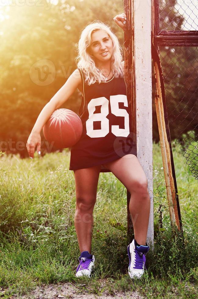 jong blond meisje met oranje basketbal poseren buitenshuis foto