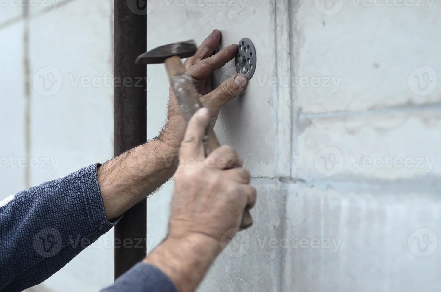 een ouderen werkman klompen een deuvel in een plastic paraplu monteren in een piepschuim muur. de werkwijze van vaststelling uitgebreid polystyreen platen. opwarming van de facade van de gebouw foto