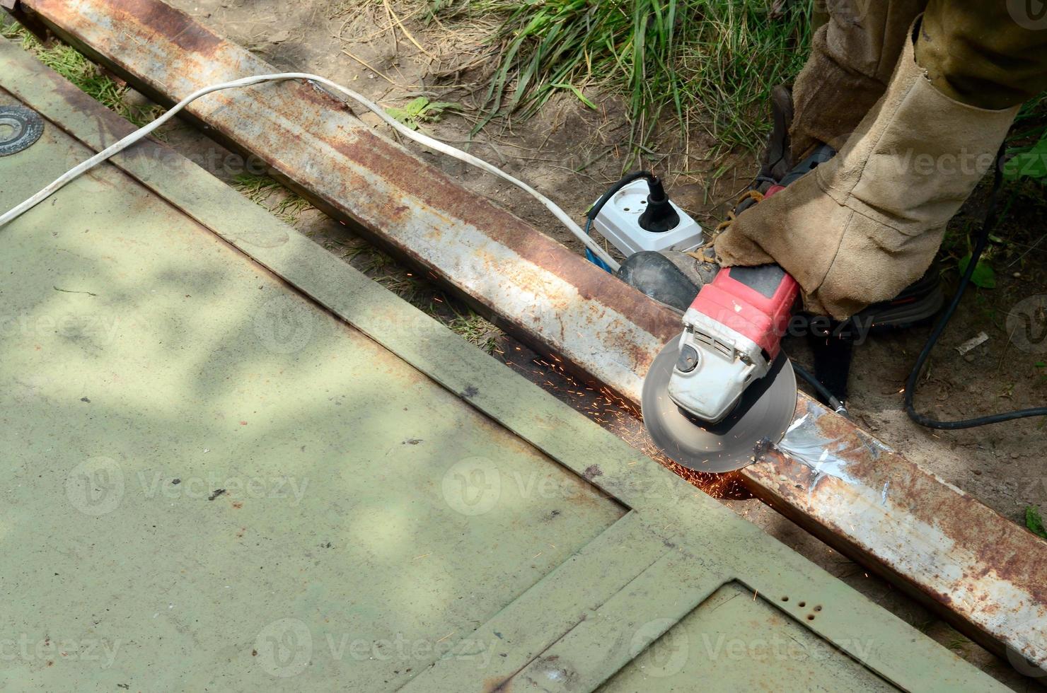 elektrisch wiel slijpen Aan staal structuur buitenshuis. oud handleiding arbeider in beschermend handschoenen snijdend metaal deur met Slijper foto