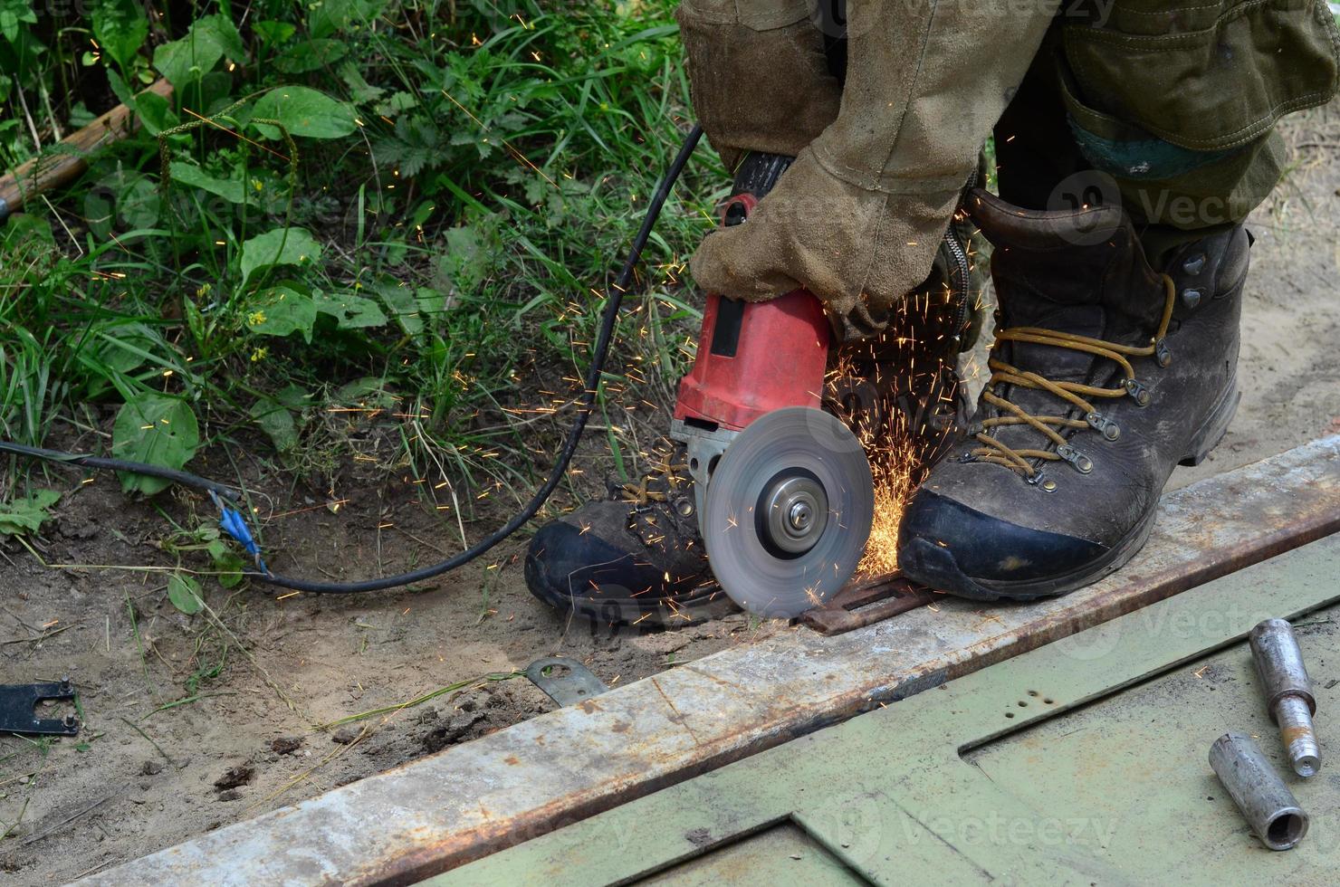 elektrisch wiel slijpen Aan staal structuur buitenshuis. oud handleiding arbeider in beschermend handschoenen snijdend metaal deur met Slijper foto