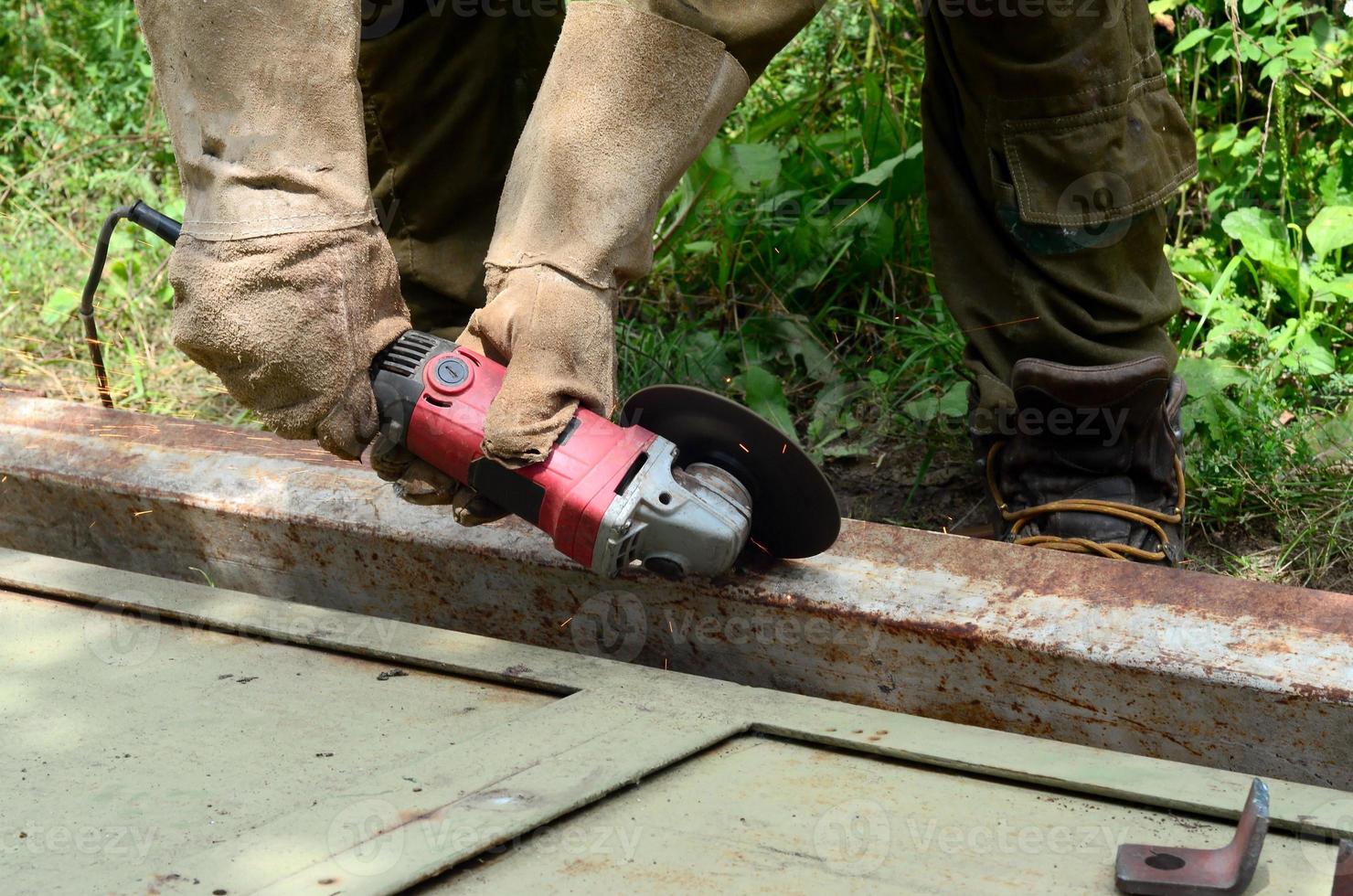 elektrisch wiel slijpen Aan staal structuur buitenshuis. oud handleiding arbeider in beschermend handschoenen snijdend metaal deur met Slijper foto