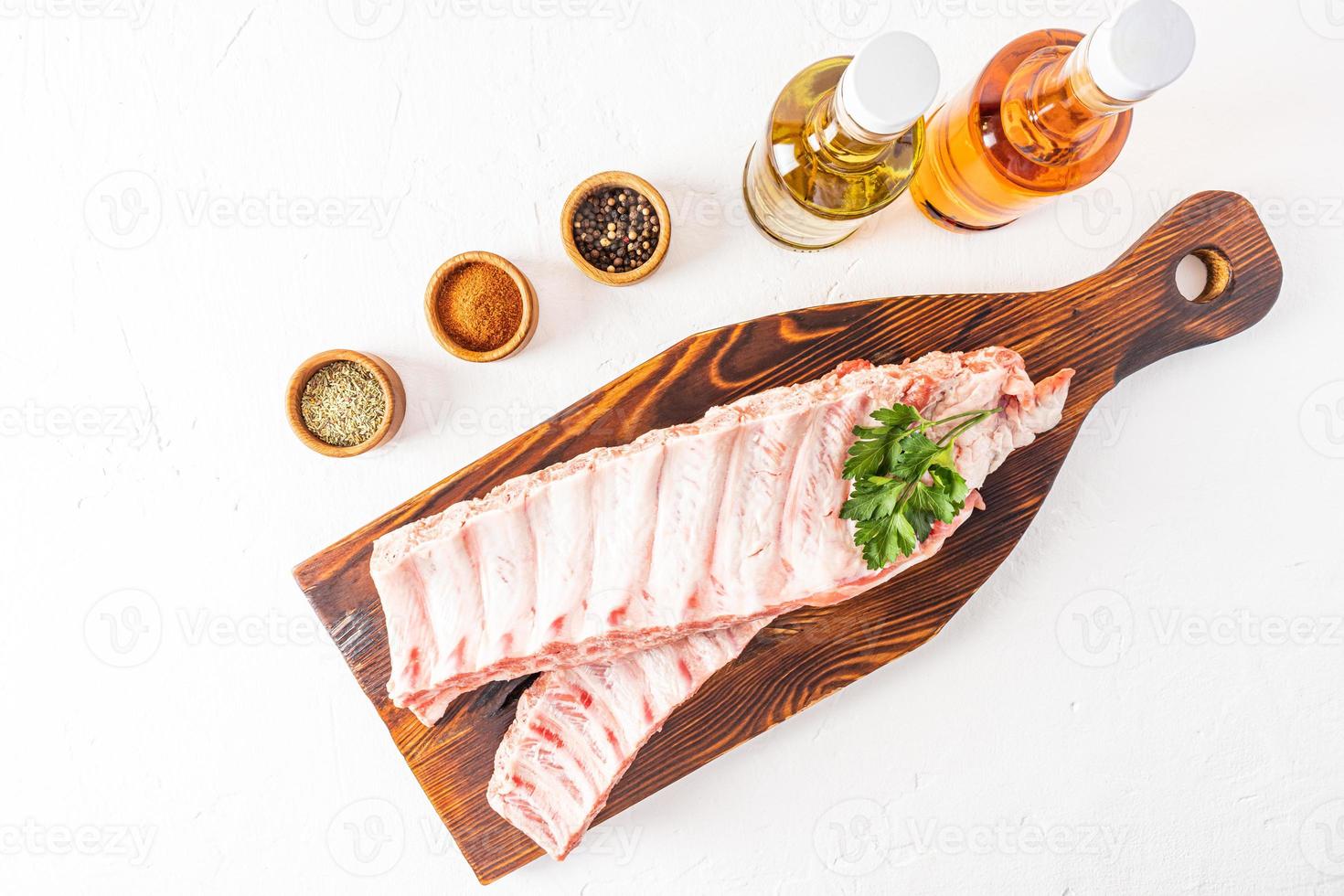 rauw boerderij varkensvlees ribben Aan een houten donker snijdend bord omringd door specerijen in marinade kommen. wit achtergrond. foto