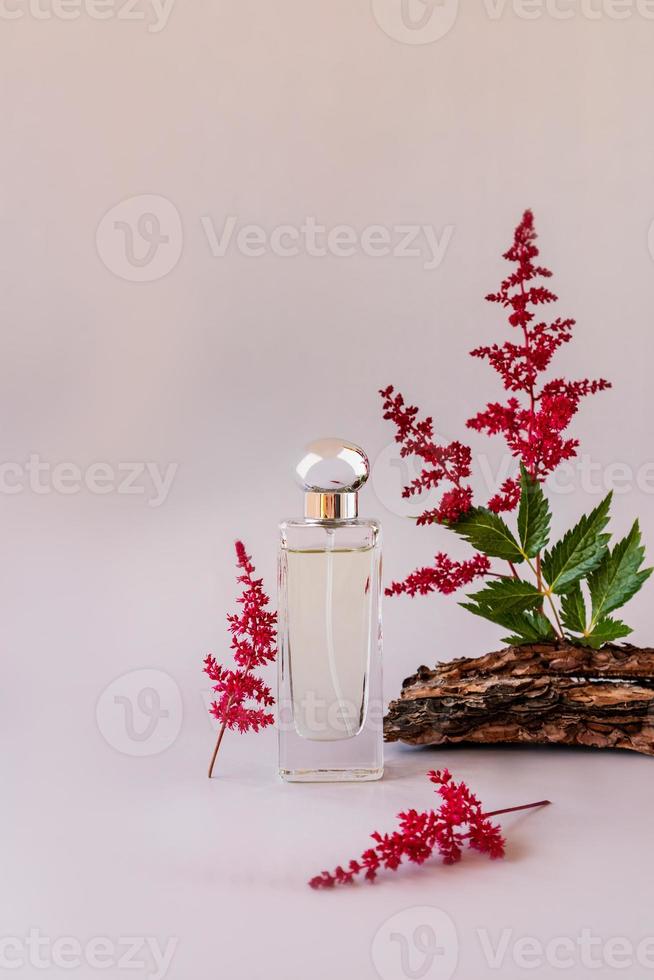 voorkant visie van een elegant fles van vrouwen parfum met takjes van roze astilbe en boom blaffen. neiging concept van natuurlijk materialen. reclame. foto