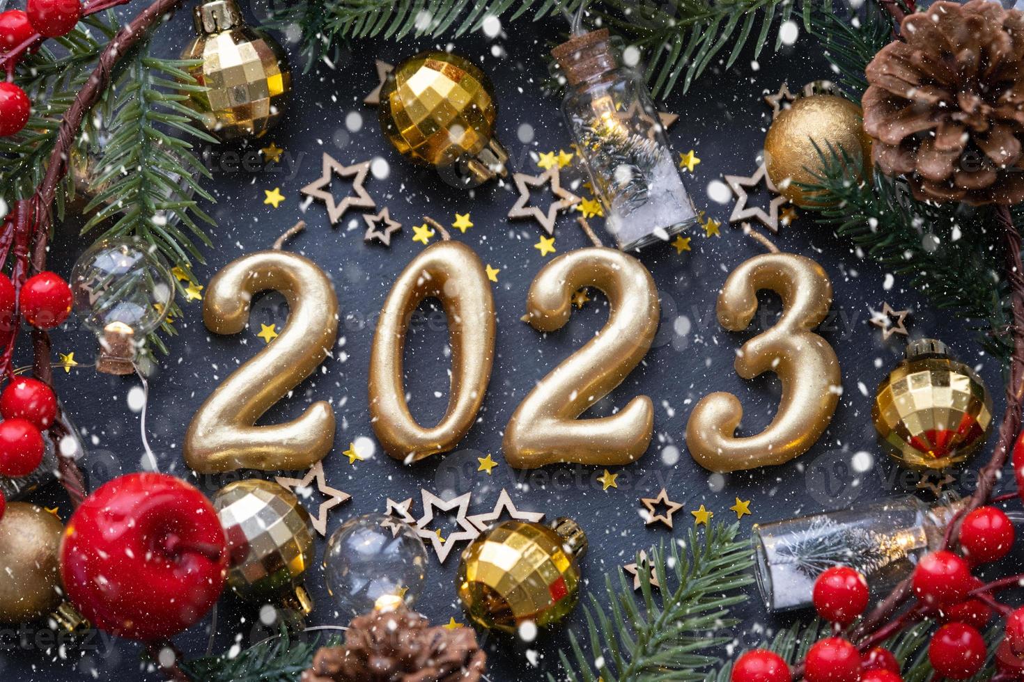 de gouden figuren 2023 gemaakt van kaarsen Aan een zwart steen leisteen achtergrond zijn versierd met een feestelijk decor van sterren, pailletten, Spar takken, ballen en slingers. groet kaart, gelukkig nieuw jaar. foto