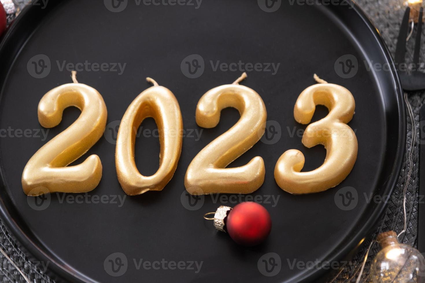gouden figuren 2023 van kaarsen Aan een zwart bord Aan een feestelijk tafel met een nieuw jaar portie. loft-stijl interieur, partij, feest. rieten servet, vork, mes foto