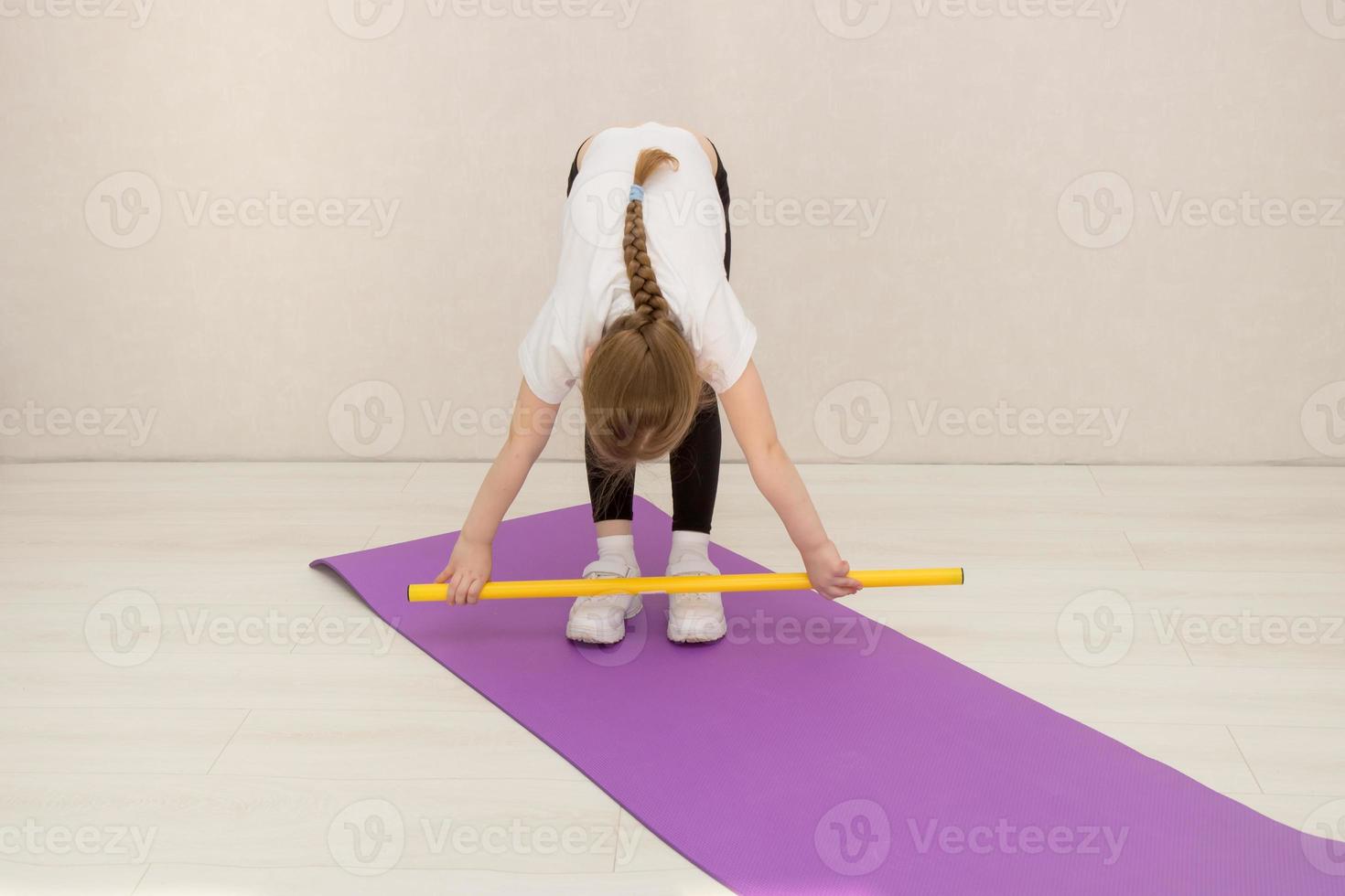 weinig meisje presteert opdrachten met een gymnastiek- stok, buigen naar beneden met een stok in haar handen foto