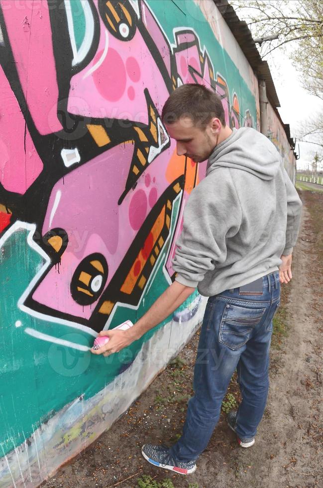 een jong vent in een grijs capuchon verven graffiti in roze en groen c foto