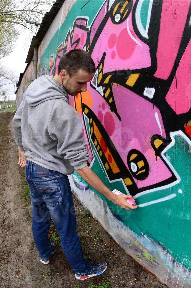 een jong vent in een grijs capuchon verven graffiti in roze en groen c foto