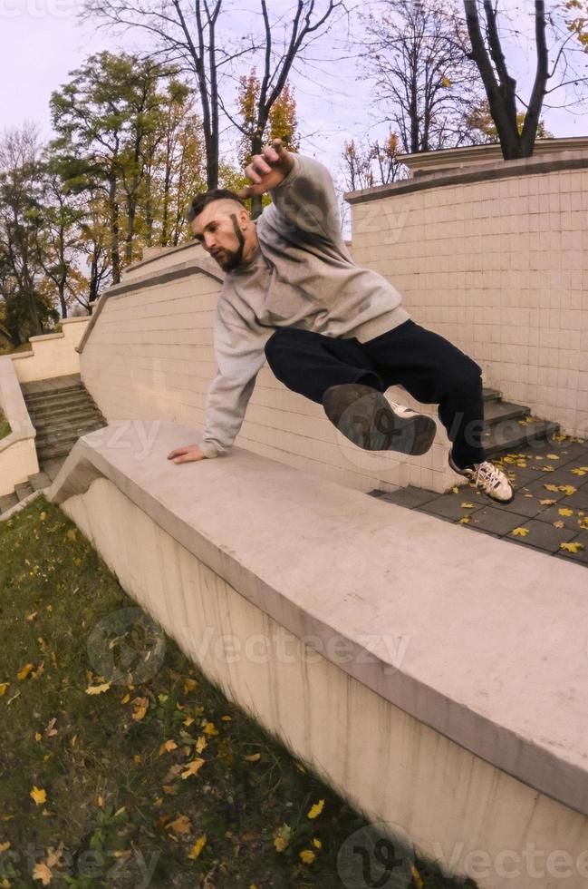 een jong vent presteert een springen door de beton borstwering. de atleet praktijken parkour, opleiding in straat conditie. de concept van sport- subculturen tussen jeugd foto