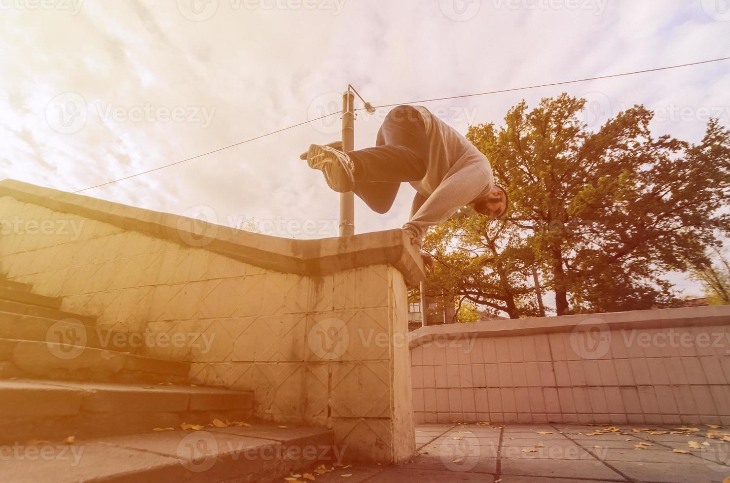 een jong vent presteert een springen door de beton borstwering. de atleet praktijken parkour, opleiding in straat conditie. de concept van sport- subculturen tussen jeugd foto