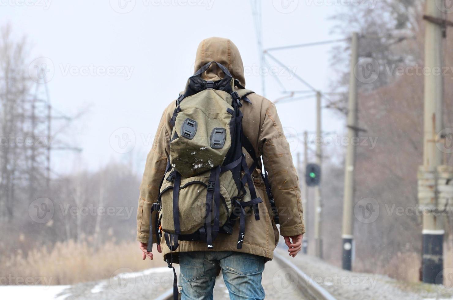 een Mens met een groot rugzak gaat verder Aan de spoorweg bijhouden duri foto