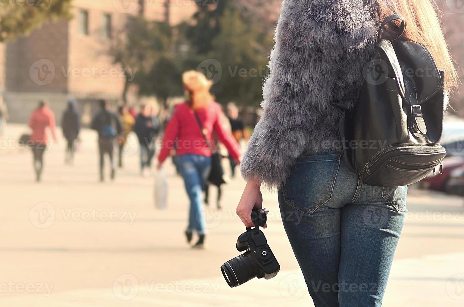 achterzijde visie van een meisje met een digitaal camera Aan een druk straat ba foto