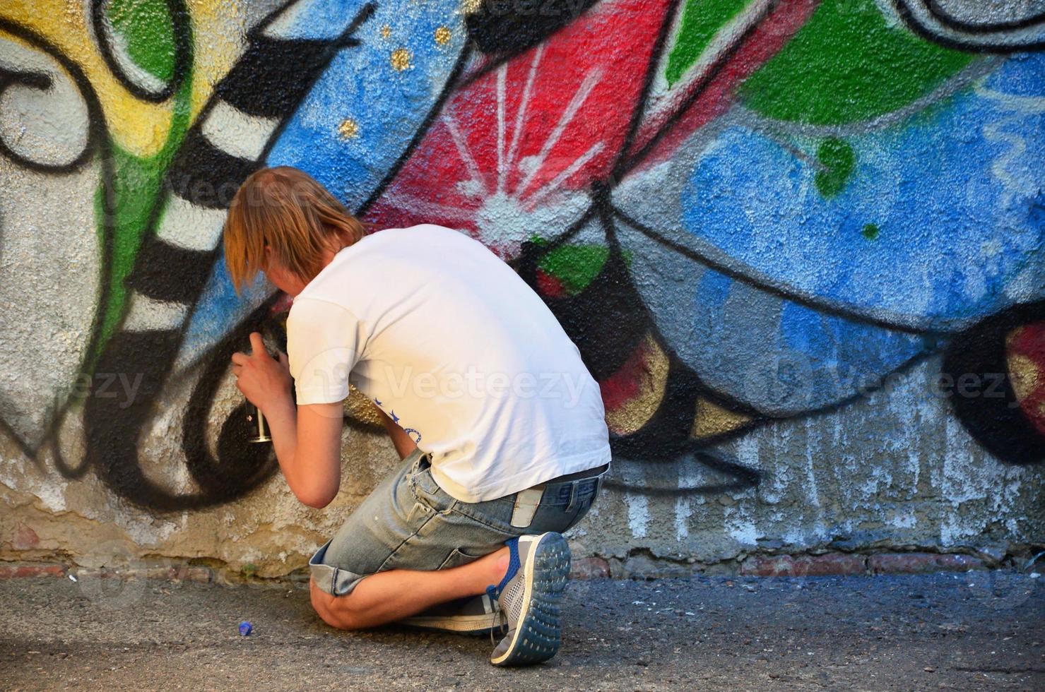 foto in de werkwijze van tekening een graffiti patroon Aan een oud beton muur. jong langharig blond vent trekt een abstract tekening van verschillend kleuren. straat kunst en vandalisme concept