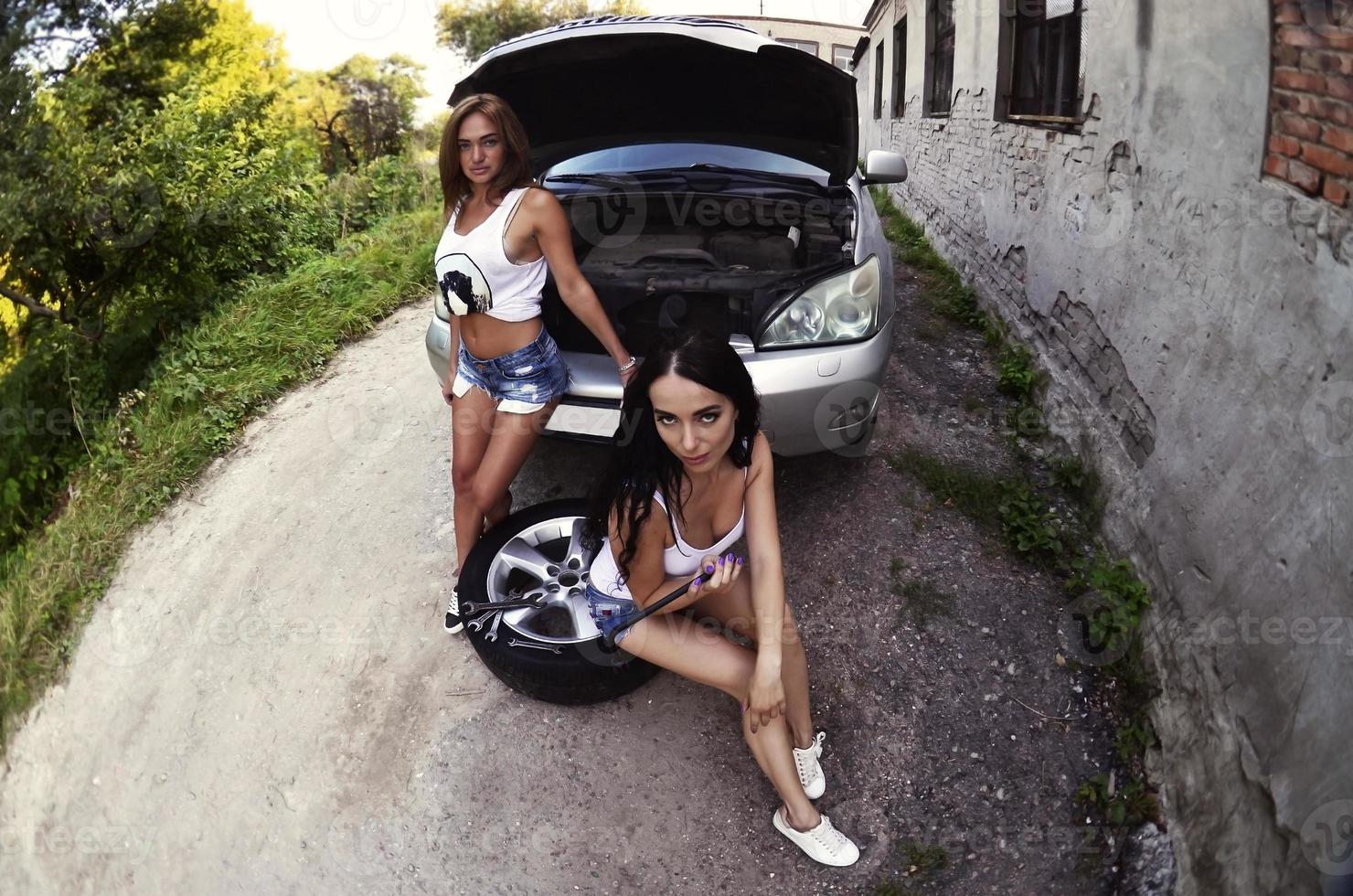 twee jong en sexy meisjes met wiel sleutels in de omgeving van een zilverachtig ca foto