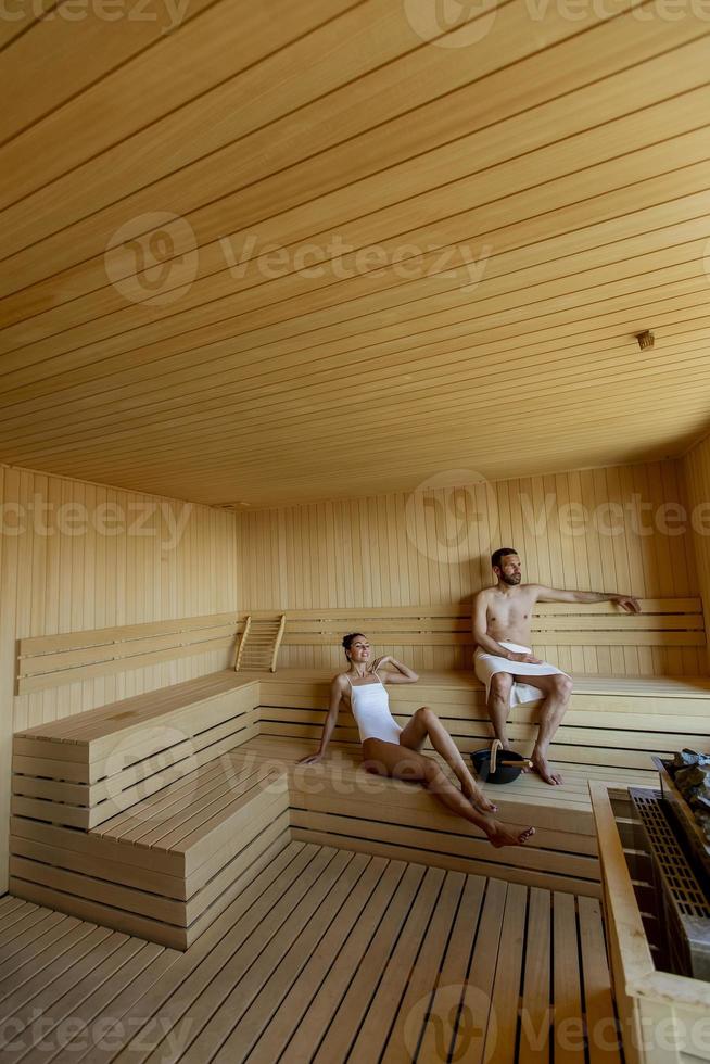 jong koppel ontspannen in de sauna en kijken naar het winterbos door het raam foto