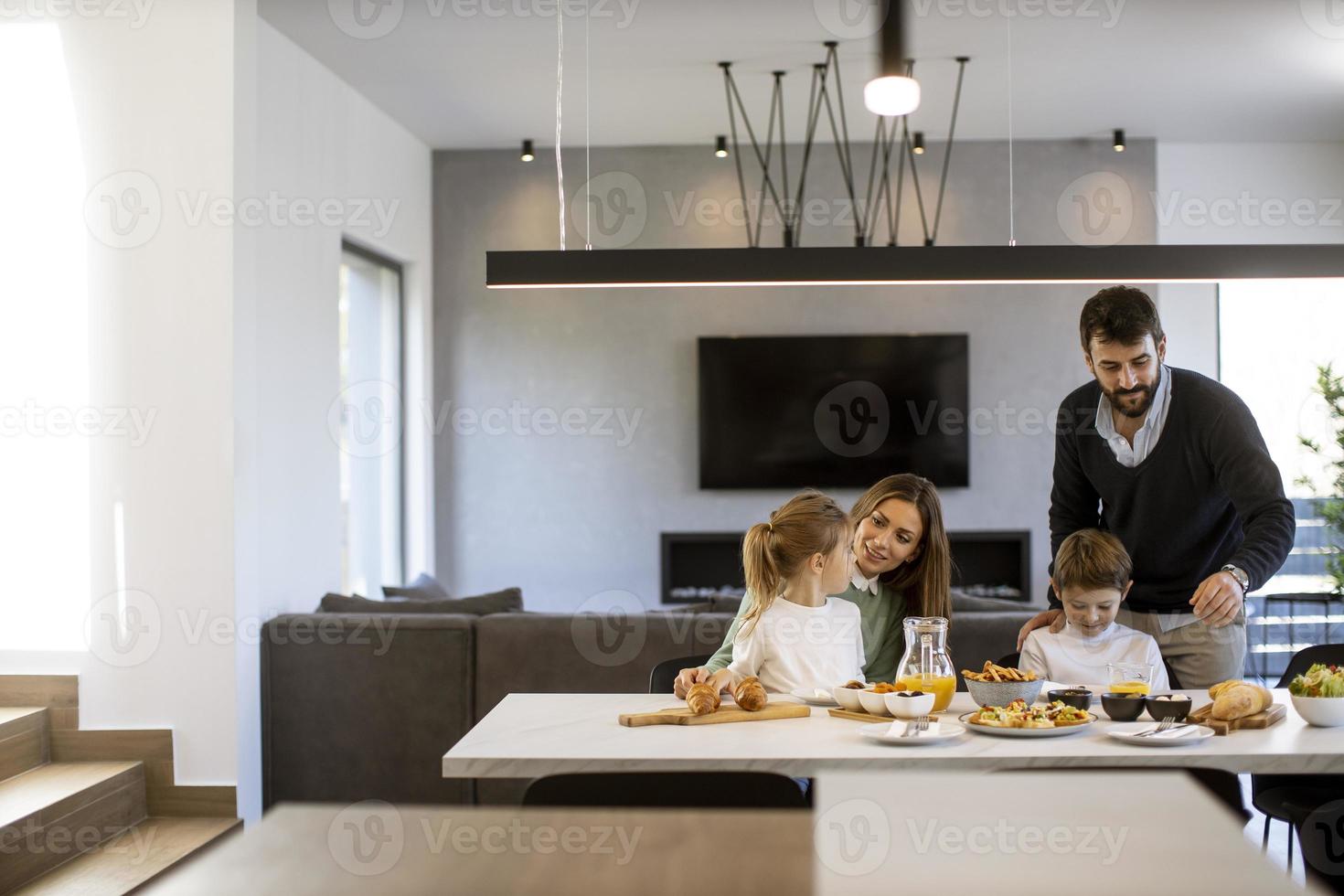 jong gelukkig familie pratend terwijl hebben ontbijt Bij dining tafel foto