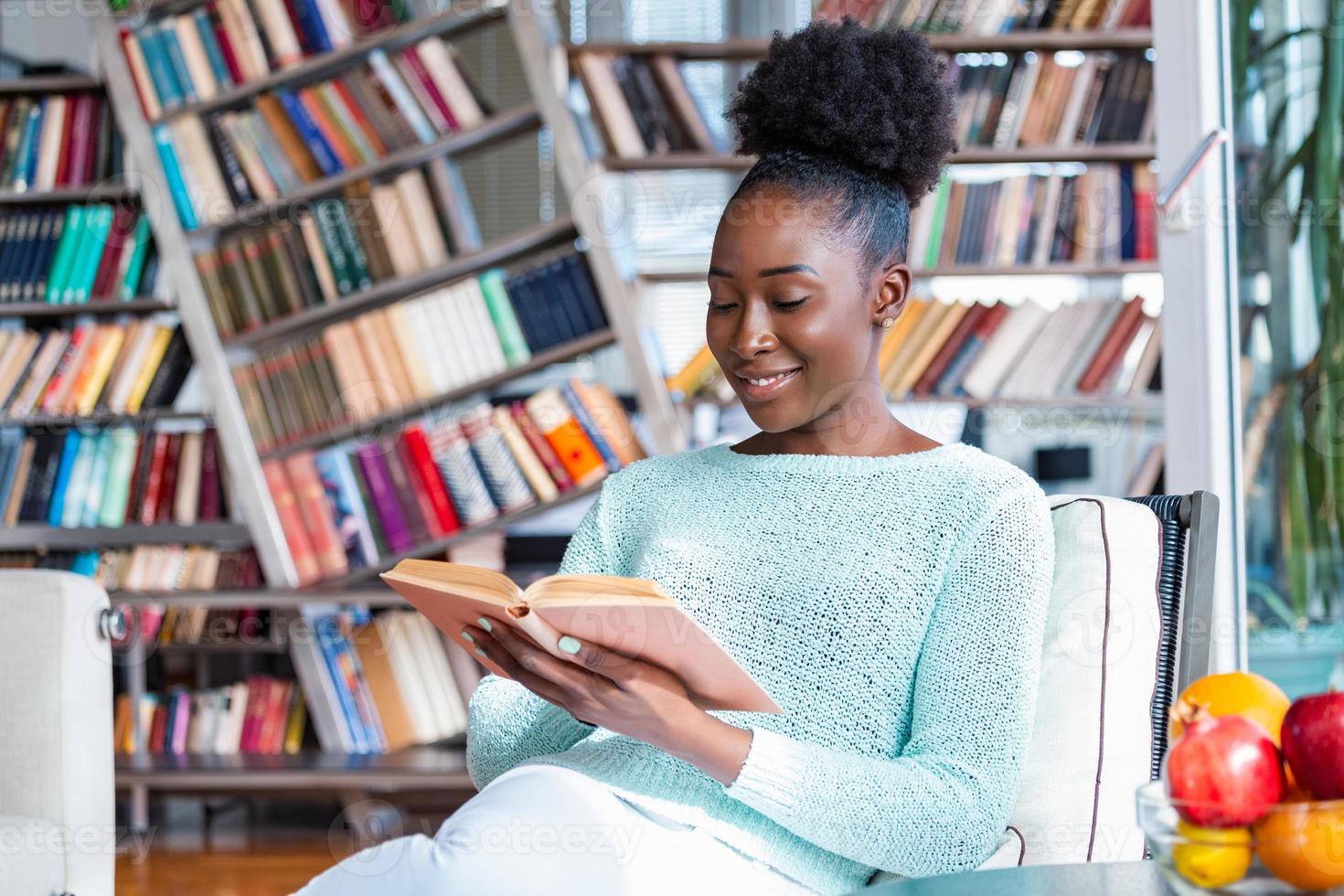 In voordeel Getalenteerd jong mooi Afrikaanse Amerikaans meisje lezing een boek Aan de bankstel met  de bibliotheek boekenkasten in de rug. mooi vrouw Aan een wit sofa lezing  een boek 15746210 Stockfoto