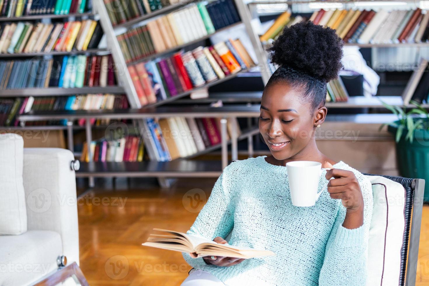 Afrikaanse Amerikaans meisje lezing een boek glimlachen gelukkig en ontspannen Aan een vrije tijd dag Bij huis. huis bibliotheek met boekenkasten in de rug. foto