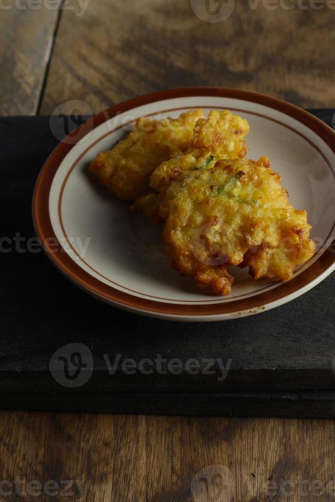 bakwan jagung of maïs beignets is Aan een zwart snijdend bord tegen een houten achtergrond foto