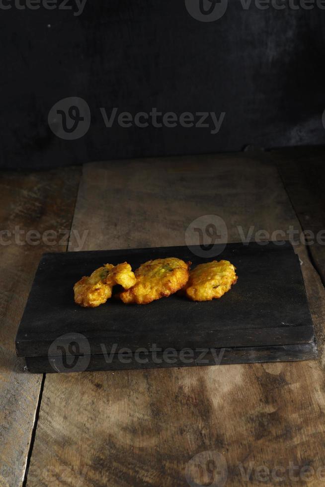 bakwan jagung of maïs beignets is Aan een zwart snijdend bord tegen een houten achtergrond foto