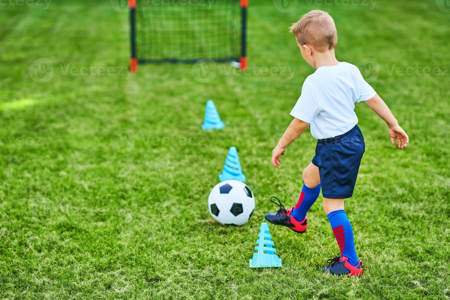 weinig jongen beoefenen voetbal buitenshuis foto