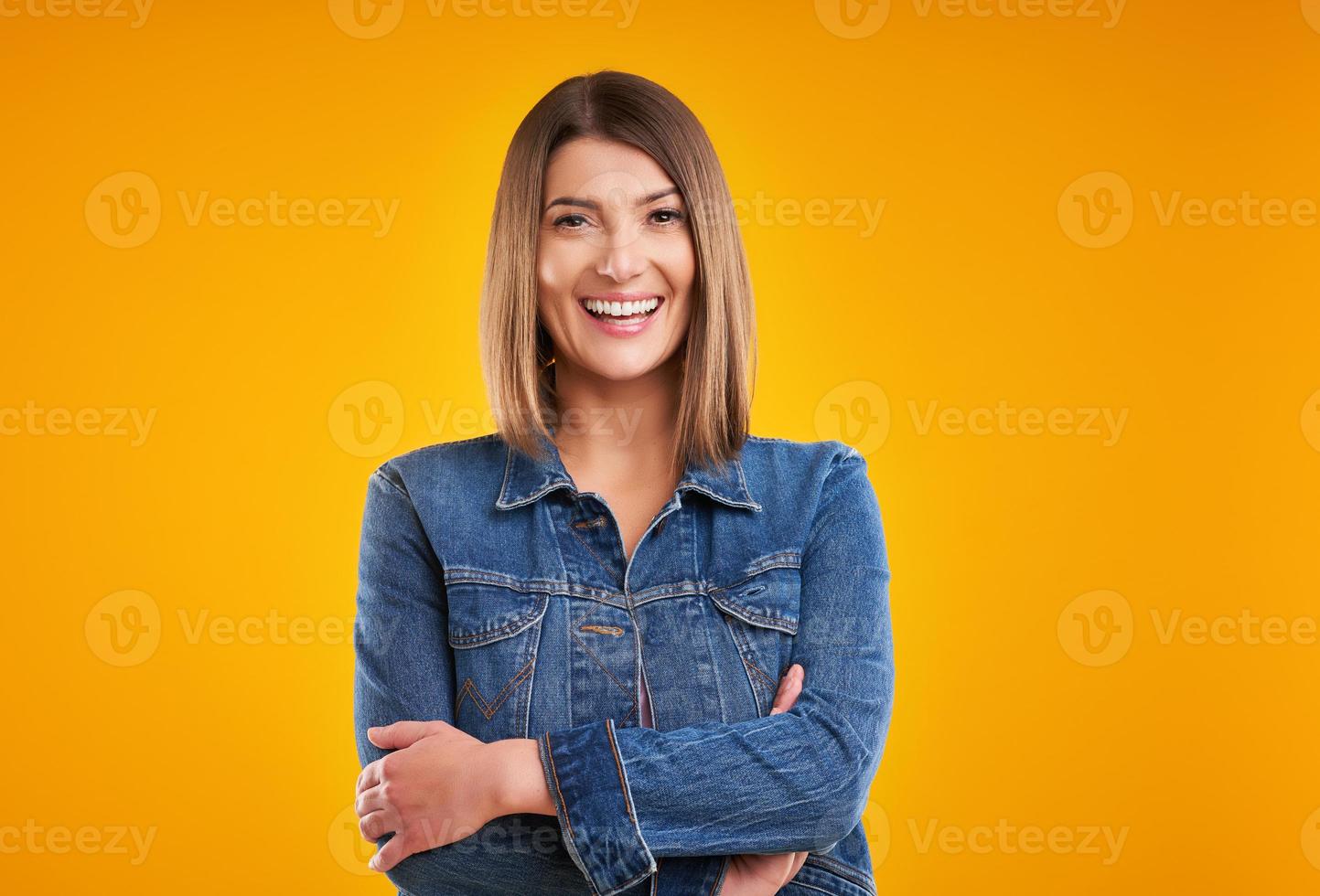 dichtbij omhoog van vrouw in denim jasje op zoek Bij camera over- geel achtergrond foto