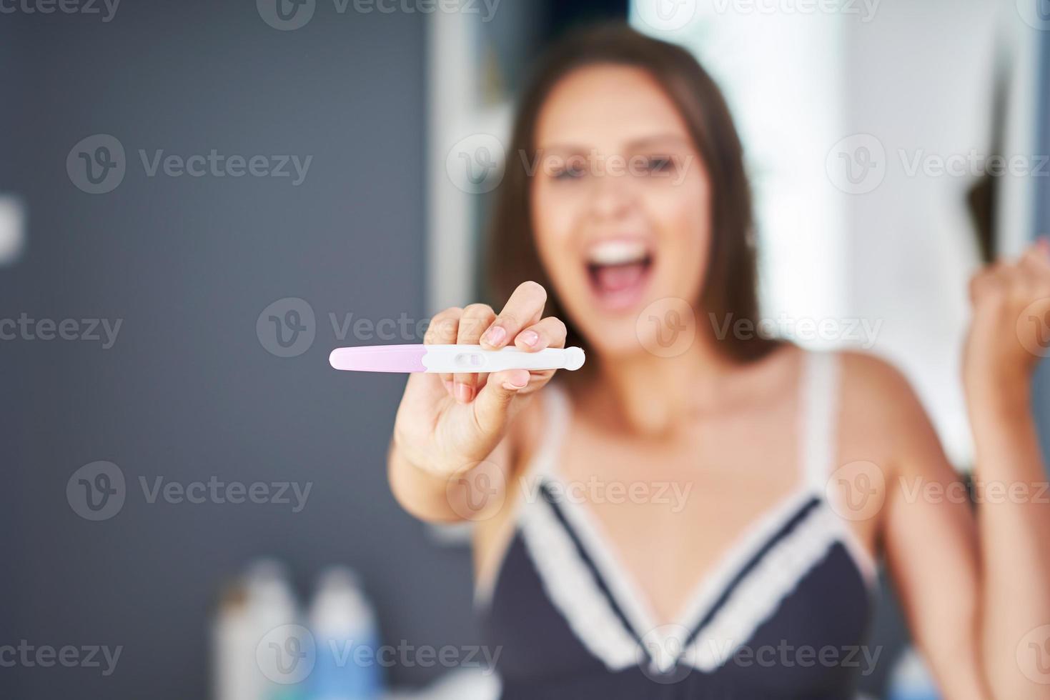 portret van gelukkig jong vrouw met zwangerschap test in de badkamer foto
