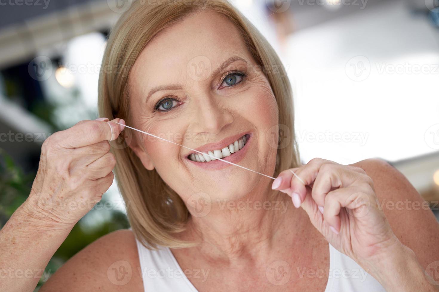 senior vrouw gebruik makend van tandheelkundig floss in de badkamer foto