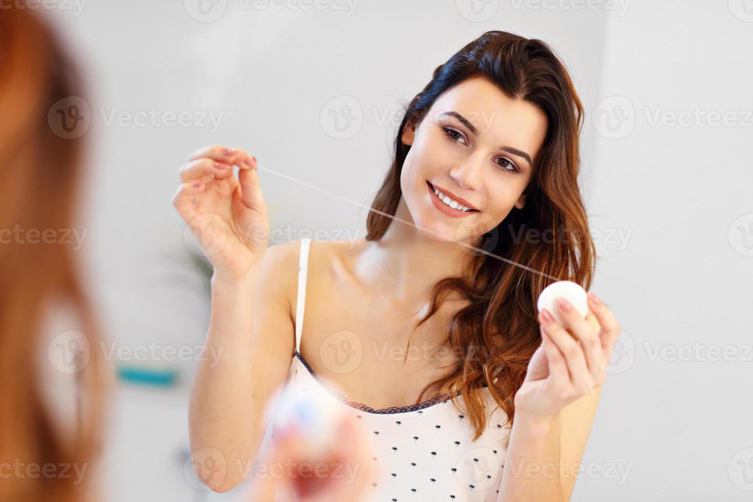 jong vrouw gebruik makend van tandheelkundig floss in badkamer foto