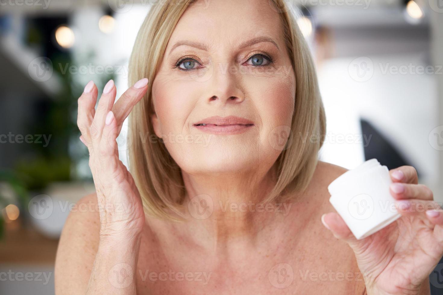 senior vrouw gebruik makend van anti rimpel room in de badkamer foto