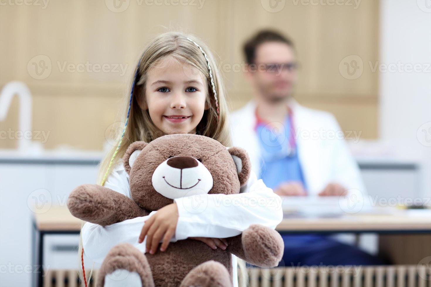 weinig meisje in kliniek met kinderarts in de achtergrond foto